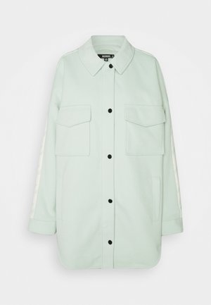 Veste-chemise à manches longues vert clair avec boutons noirs, deux poches à rabat devant, poches latérales et un col.
