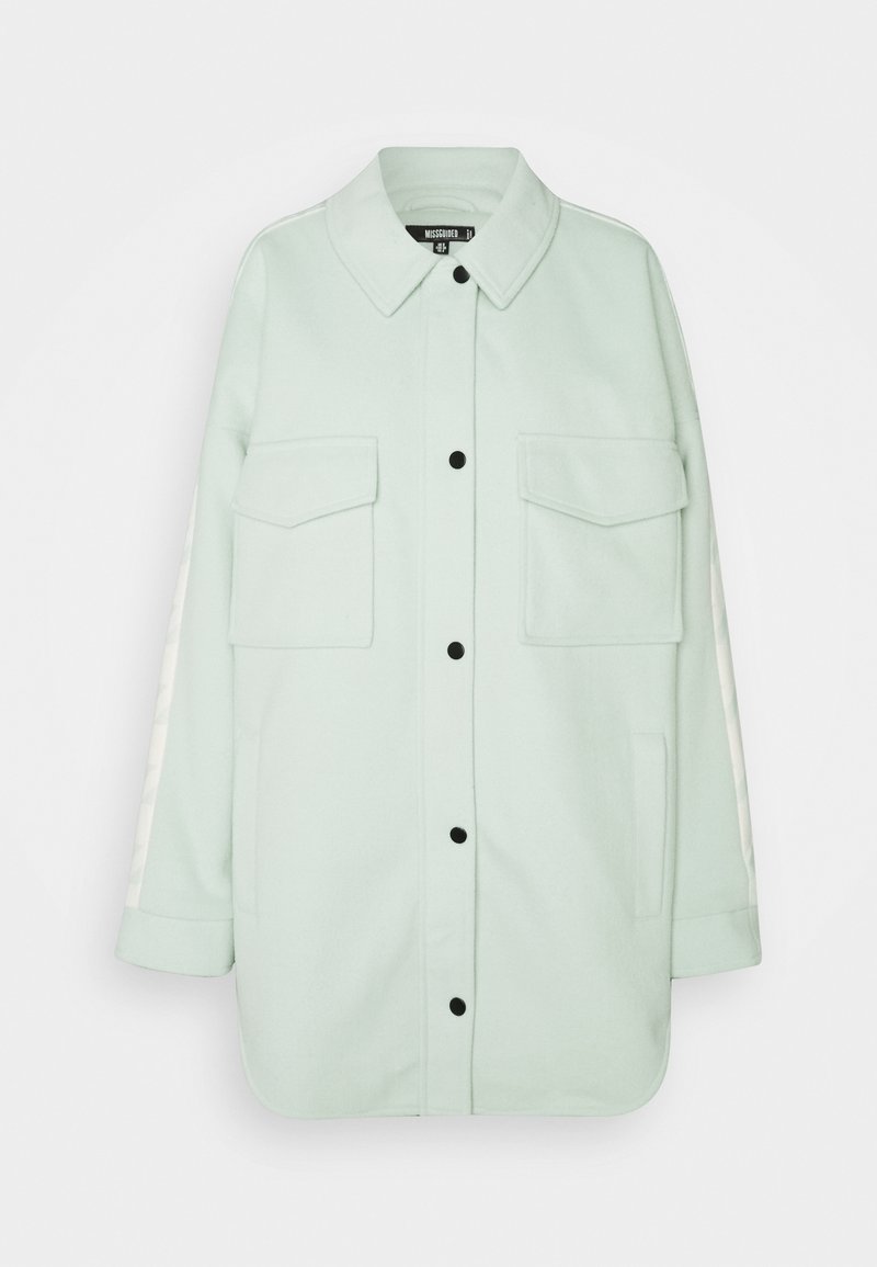 Veste-chemise à manches longues vert clair avec boutons noirs, deux poches à rabat devant, poches latérales et un col.