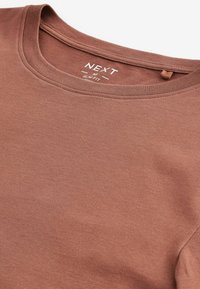 Tricou slim fit într-o nuanță de maro discret, realizat din bumbac moale, având un guler rotund și detalii subtile de cusătură pe guler.