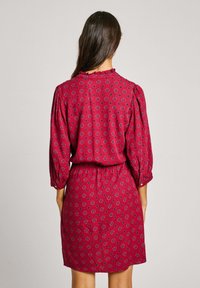 Vestido rojo con estampado, de manga larga, con puños recogidos y cintura ajustada. Presenta un escote redondo y un motivo floral en toda su superficie.