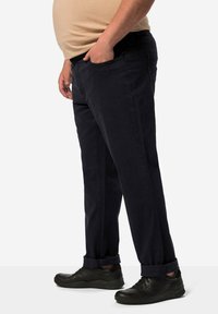 Jeans de mezclilla azul oscuro con un corte recto, que cuentan con bolsillos laterales y puños enrollados. Combinados con zapatillas deportivas negras.