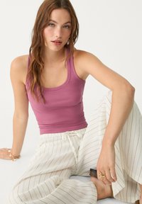 Rosa gerippter Tanktop kombiniert mit cremefarbenen weit geschnittenen gestreiften Hosen. Bemerkenswerte Details sind ein Kordelzugbund und eine strukturierte Stoffoberfläche.