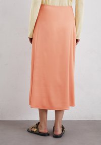 Gonna midi in satin pesca con una texture liscia, una silhouette fluida e una leggera lucentezza. Abbinata a sandali neri a piatto con dettagli dorati.