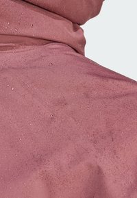 Vandafvisende pink stof med en glat tekstur, der har dråber på overfladen, hvilket indikerer fugtafvisende egenskaber.