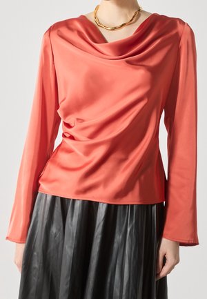 Top a maniche lunghe color corallo in un tessuto morbido, abbinato a una gonna in pelle nera plissettata. Accentuato da una collana in oro.