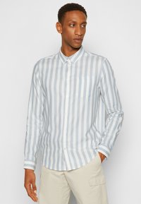 Camicia button-up a righe blu chiaro e bianche con maniche lunghe, colletto e tasca sul petto, caratterizzata da un orlo curvo e una texture di tessuto morbido.