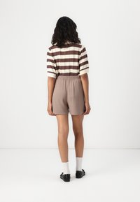 Pull tricot rayé en crème et marron, avec des manches courtes, associé à un short marron avec une taille élastique.