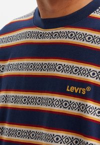 Námorně modré tričko s vodorovnými pruhy v červené, žluté a krémové barvě, s geometrickým vzorem a žlutým logem "Levi's".