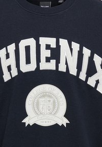 Tengerészkék pulóver, fehér hímzett "PHOENIX" felirattal és a középen "COLLEGE OF ARTS" felirattal ellátott kör alakú dizájnnal. Puha tapintású.