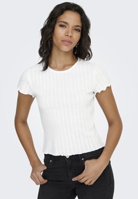 Witte geribbelde top met korte mouwen, met geschulpte randen en een aangesloten ontwerp, gedragen met zwarte jeans; heeft een ronde halslijn en een subtiele textuur.