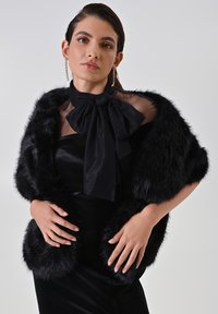 Wrap in pelliccia sintetica nera con maniche corte, dotato di un fiocco trasparente nero e un vestito aderente nero sottostante. Texture liscia, design elegante.