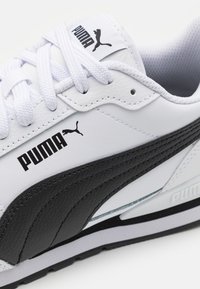 Valkoinen ja musta urheilukenkä, jossa on synteettisestä nahasta valmistettu päällinen, teksturoituja mustia yksityiskohtia ja valkoiset nauhat. Sivussa on PUMA logo.