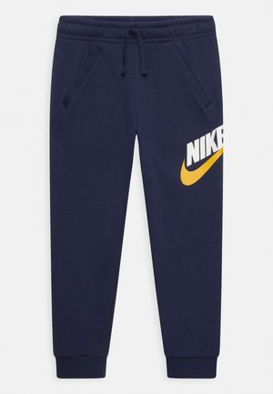 Granatowe spodnie dresowe Nike z elastycznym pasem i sznurkiem, kieszeniami bocznymi, mankietami przy kostkach oraz białym i żółtym logo Nike na prawej udzie.