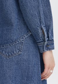 Jeansskjorta med långa ärmar, blå nyans och knappmanchett. Har en bakficka med kontrasterande söm och en texturerad yta.