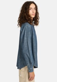 Blauwe chambray shirt met lange mouwen, knoopsluiting bij de mouwen en een iets gebogen zoom. Soepele textuur, klassieke kraagontwerp, lichtgewicht materiaal.