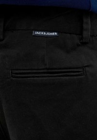 Pantalon noir avec une coupe ajustée, texture lisse et une poche arrière unique avec une couture horizontale. L'étiquette indique "JACK & JONES."