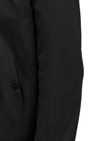 Zwarte jas met een gladde, matte textuur. Voorzien van een zijzak met een knoopsluiting. Ontwerpaccenten zijn onder andere strakke lijnen en minimalistische details.