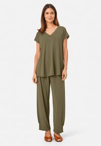 Oliwkowa, krótko rękawowa bluzka z dekoltem w serek o luźnym kroju, w komplecie z dopasowanymi, szerokimi spodniami, wykonanymi z miękkiej, lekko opadającej tkaniny.
