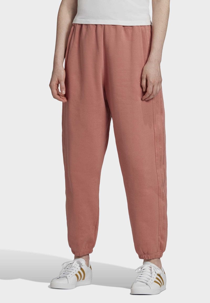 Rosa sweatpants med elastisk midja, muddar vid anklarna och sidostråk. Kombinerat med vita sneakers med guldaccenter.