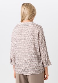 Leichte, gemusterte Bluse mit geometrischem Design in Beige und Weiß. Mit Dreiviertelärmel und rundem Kragen. Rückansicht.