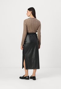 Pull en maille côtelée marron avec col associé à une jupe maxi en simili cuir noire comportant une fente sur le côté, et des chaussures noires avec des accents de boucle.