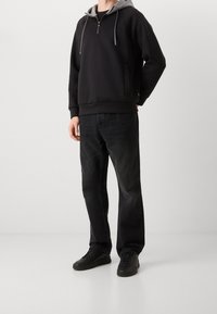 Sudadera con cremallera negra y capucha gris, que presenta un bolsillo delantero y cordones. Combinada con jeans negros rectos y zapatillas negras.