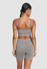Szary zestaw sportowy składający się z biustonosza i wysokich spodenek, wykonany z teksturowanej tkaniny. Posiada cienkie ramiączka i dopasowany krój.