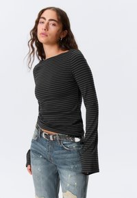 Μακρυμάνικο πουκάμισο με μαύρες και γκρι ρίγες, με στρογγυλή λαιμόκοψη, κατασκευασμένο από μαλακό υλικό. Συνδυασμένο με τζιν παντελόνι με φθαρμένο look και ζώνη με σχέδια.