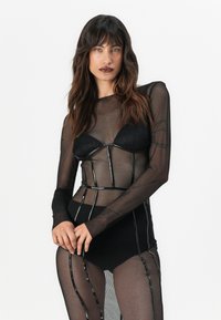 Μαύρη δικτυωτή γυναικεία φόρμα με μακριά μανίκια, που διαθέτει δομικό σχέδιο, διαφανή υφή και μεταλλικές λεπτομέρειες που ενισχύουν τη σιλουέτα.