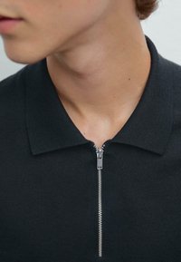 Černé polo tričko na zip s texturovanou tkaninou, strukturovaným límcem a stříbrným zipem. Detailní pohled zaměřený na oblast krku.