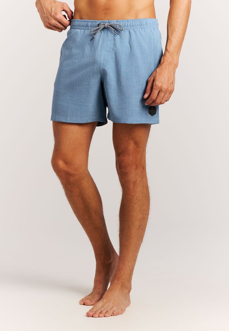 Mann trägt hellblaue Badeshorts bis zur Mitte des Oberschenkels mit schwarz-weißer Kordel und einem kleinen dunklen Fleck nahe am Saum.
