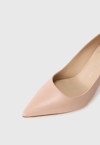 Pompe à talon aiguille nude en cuir avec une texture lisse et un design décolleté, dotée d'un intérieur beige et d'une discrète signature sur la semelle intérieure.