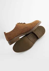 Ruske suede cipele na vezanje s zaobljenim prstom, kontrastnim šavovima i ravnim gumenim potplatom. Imaju jednostavan dizajn s minimalnim akcentima.