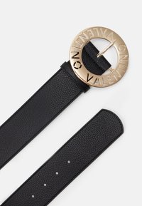 Svart läderbälte med en stor cirkulär guldfärgad spänne som har en graverad "VALENTINO" och en strukturerad rem med flera justeringshål.