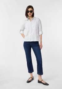 Biała i granatowa koszula w paski z podwiniętymi rękawami, zestawiona z ciemnoniebieskimi dżinsami 7/8 i czarnymi balerinami, charakteryzująca się minimalistycznym stylem.