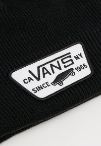 Gorro de punto negro con un parche rectangular blanco que tiene texto en negro que dice "VANS NY" y una imagen de una patineta, establecido en 1966.