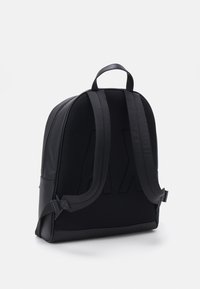 Zaino nero con pannello in rete testurizzata, dettagli in pelle liscia, spallacci imbottiti e manico superiore. Presenta una chiusura con zip e un design strutturato.