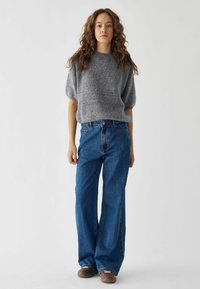 Maglione grigio a maglia con maniche corte abbinato a jeans a gamba larga blu. L'outfit presenta una vestibilità comoda e un design a maglia texturizzata.