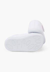 Weiße Slipper mit einer strukturierten Gummisohle, die einen glatten Stoffoberteil und einen abgerundeten Absatz aufweist. Die Sohle hat kleine Pfotenabdruckmuster.