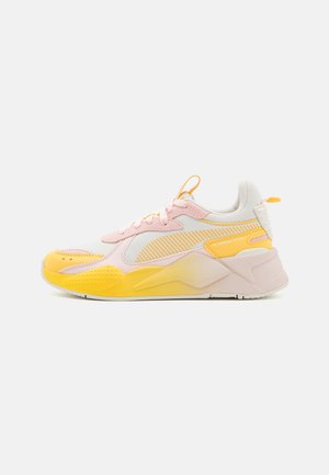 Zapatilla baja con malla blanca, superposiciones rosas, acentos amarillos, suela gruesa y lengüetas en la lengüeta y talón, mostrada en perfil derecho.