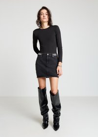 Body noir à manches longues associé à une mini-jupe en denim noir avec des accents cloutés à la taille, complétés par des bottes noires brillantes montant jusqu'aux genoux.