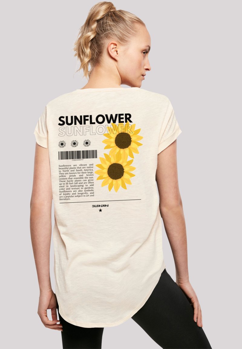 Cream-colored short-sleeve t-shirt featuring a sunflower graphic, black text, and a barcode on the back; curved hemline.