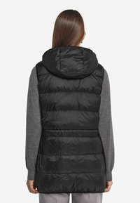 Czarna, pikowana kamizelka z kapturem o eleganckim designie i wypchanej fakturze. Widziana z tyłu kamizelka prezentuje dopasowaną sylwetkę oraz gładkie wykończenie.