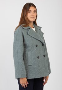 Cappotto doppiopetto in morbido tessuto azzurro chiaro con texture; presenta bottoni neri, colletto a rever e tasche laterali.