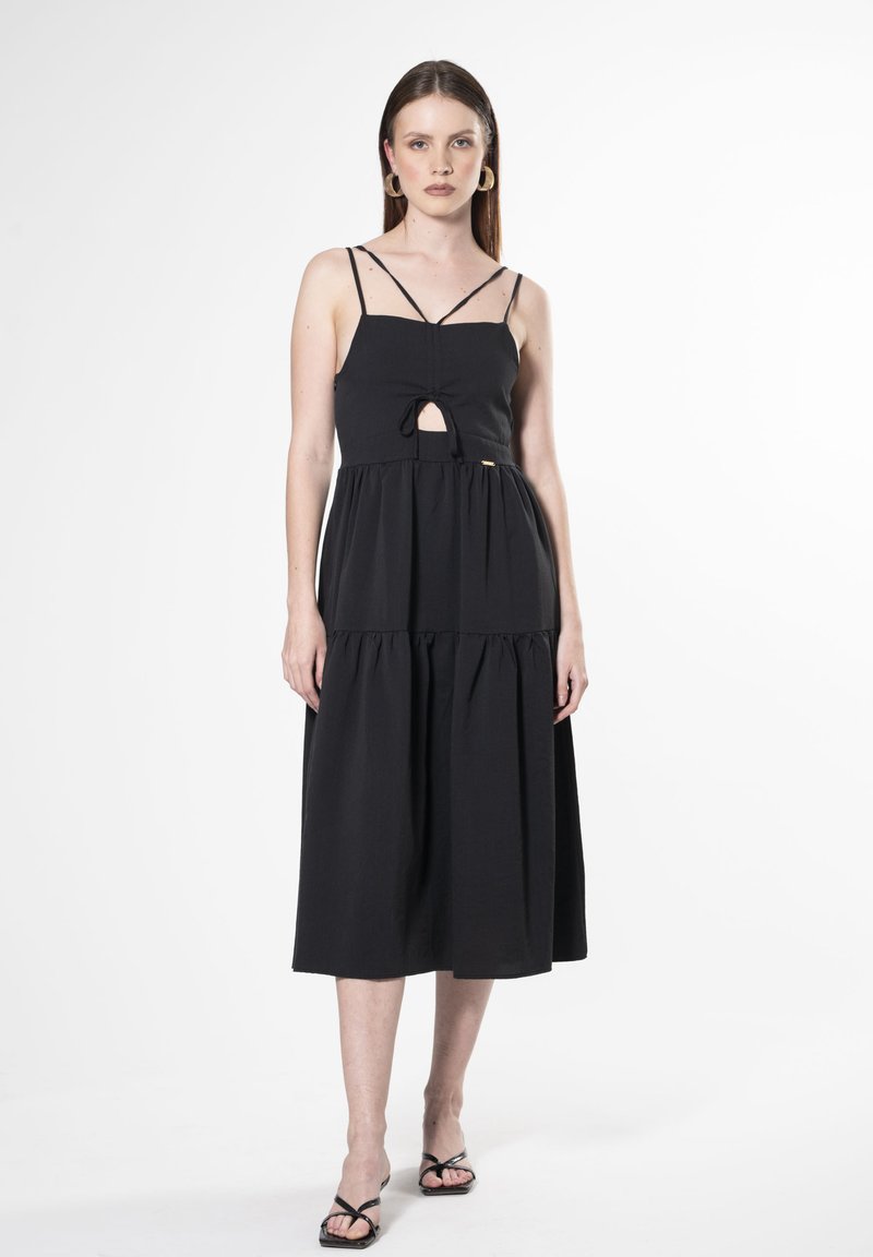 Vestido midi negro con tirantes finos, detalle de corte en forma de llave en el frente y falda de capas acampanadas. Textura suave, diseño sencillo.