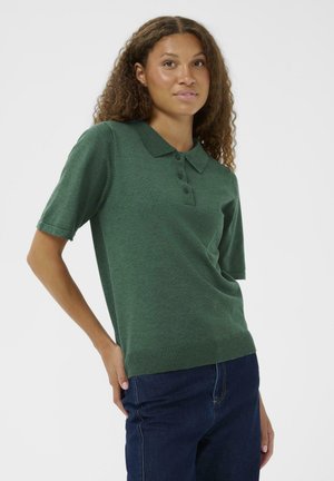 Grünes kurzärmliges Poloshirt aus strukturiertem Strick, mit einer Dreiknopfleiste und geripptem Saum, kombiniert mit dunkelblauen Jeans.