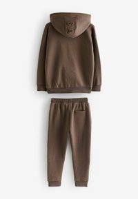 Brun hættetrøje og matchende sweatpants lavet af blødt stof. Hættetrøjen har et logo på ryggen, elastiske manchetter og en kænguru-lomme.