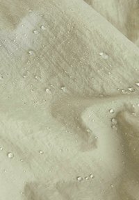 Beżowy, wodoodporny materiał o teksturowanej powierzchni, z małymi kroplami wody rozsianymi po nim, podkreślającymi jego właściwości odporne na wilgoć.