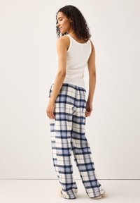 Vit ribbad linne topp som matchas med blå och vita rutiga pyjamasbyxor med lös passform och elastisk midja. Mjuk textur är synlig.