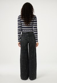Zwarte wijde jeans met witte kraalaccenten en twee achterzakken, gecombineerd met een gestreepte marineblauwe en witte lange mouwtop met geribbeld textuur.